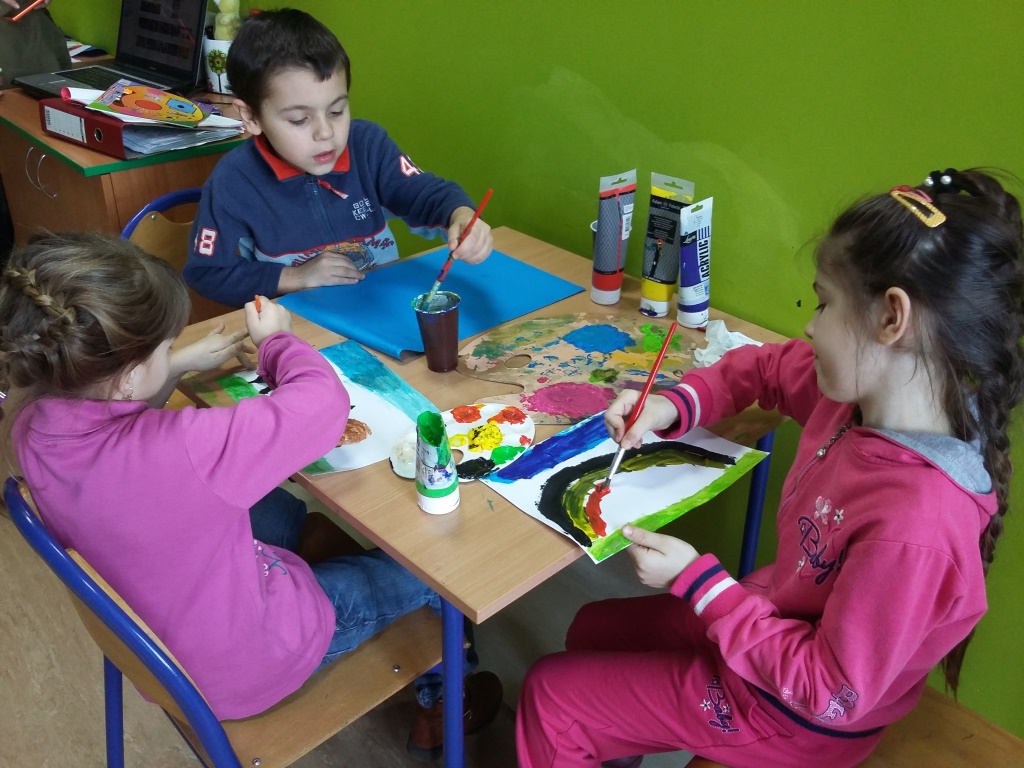 Zdjęcie przedstawia dzieci z placówki malujące obrazy farbami na kartkach.
