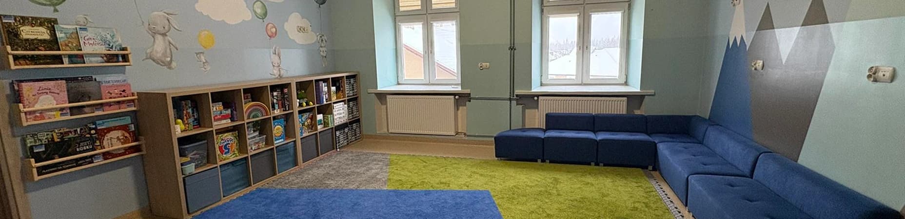 Sala zabaw dla dzieci, szafki, kanapa oraz kolorowy dywan.