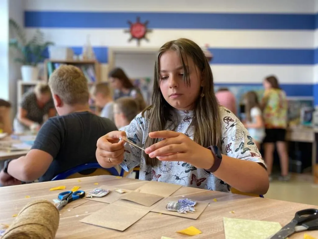 Dziecko tworzące dekorację, w tle inne dzieci i ściana w paski