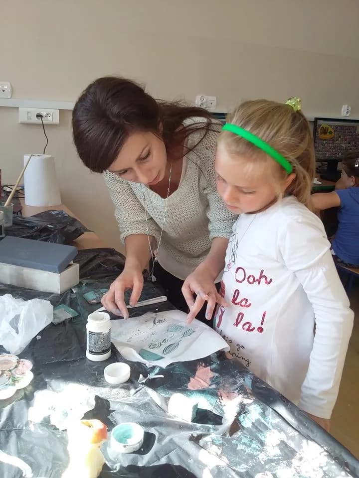 Zdjęcie przedstawia dziewczynkę oraz opiekunkę podczas warsztatów Kraina Rozmaitości razem tworzących rękodzieła przy stole z czarnym nakryciem.