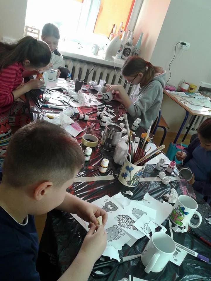 Zdjęcie przedstawia dzieci z placówki przy stole z czarnym nakryciem malujące na porcelanie.