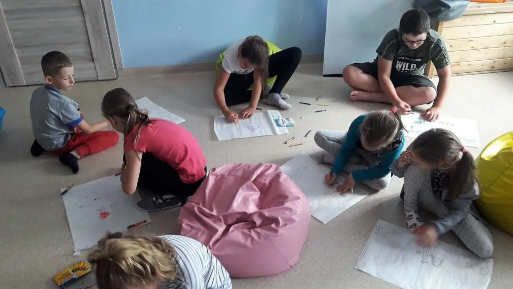 Obraz przedstawia wychowanków SPWD podczas warsztatów relaksacyjnych. Na zdjęciu możemy ujrzeć dzieci rysujące muzykę.