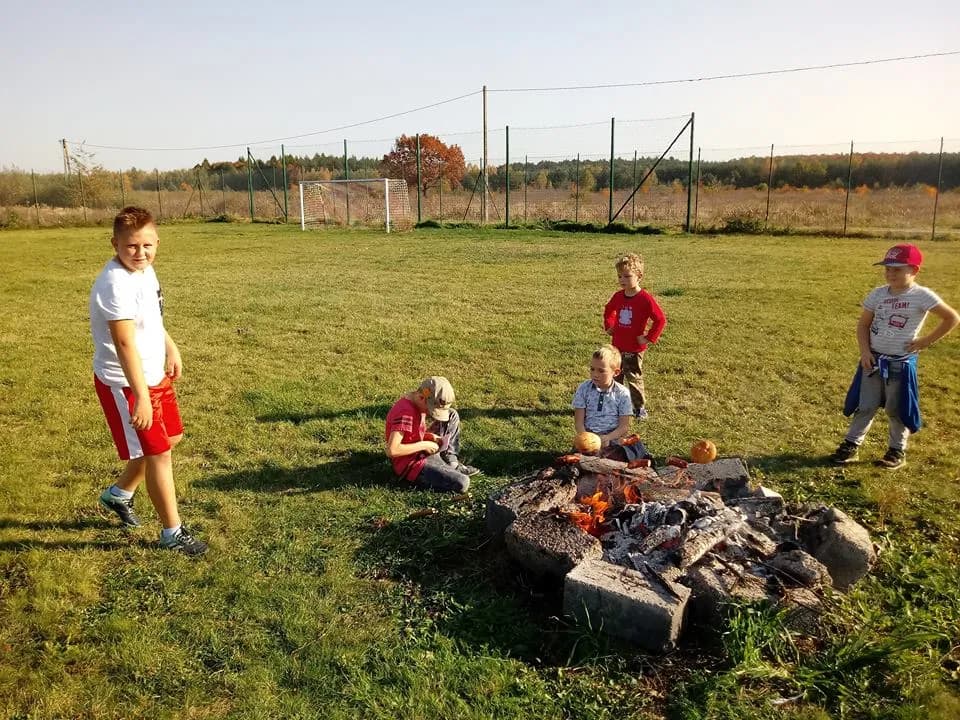 Obraz przedstawia wychowanków oraz ognisko na boisku.