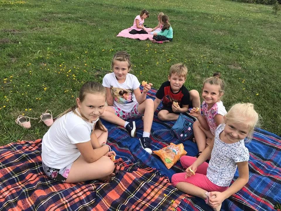 Zdjęcie przedstawia dzieci siedzące na kocach położonych na trawie podczas pikniku.