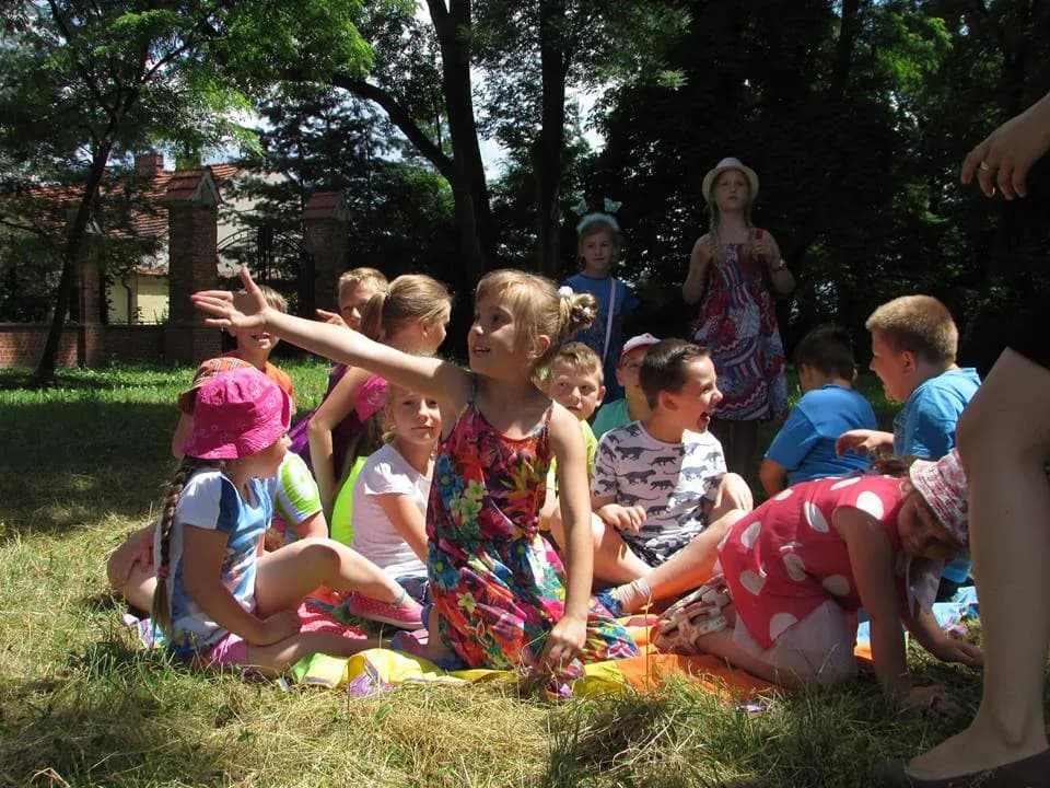 Zdjęcie przedstawia dzieci z placówki na zewnątrz w otoczeniu drzew podczas warsztatów z komunikacji