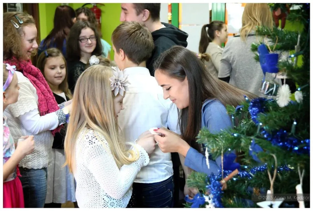Zdjęcie przedstawia dzieci z placówki oraz pracowników na wspólnej wigilii składających sobie życzenia i dzielących się opłatkiem.