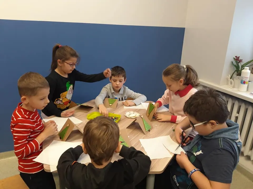 Obraz przedstawia wychowanków podczas zajęć artystycznych. Na których pracują przy użyciu techniki scrapbookingu wykonując kartki piankowo-brokatowe.