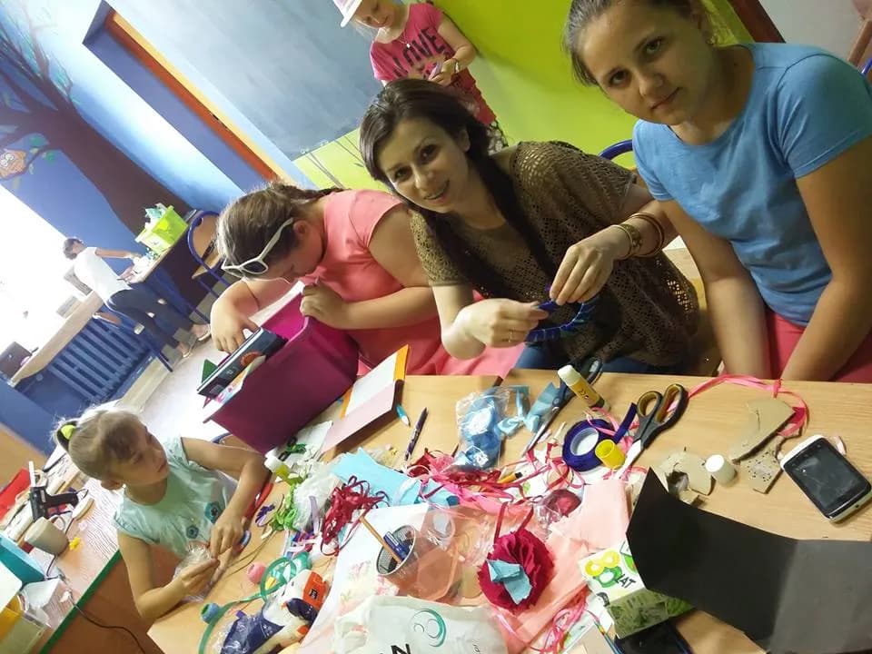 Zdjęcie przedstawia dzieci i pracowników placówki przy stole robiących rękodzieła.
