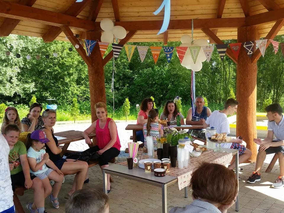 Zdjęcie przedstawia ludzi pod drewnianym zadaszeniem podczas grilla z okazji Dnia Rodziny.