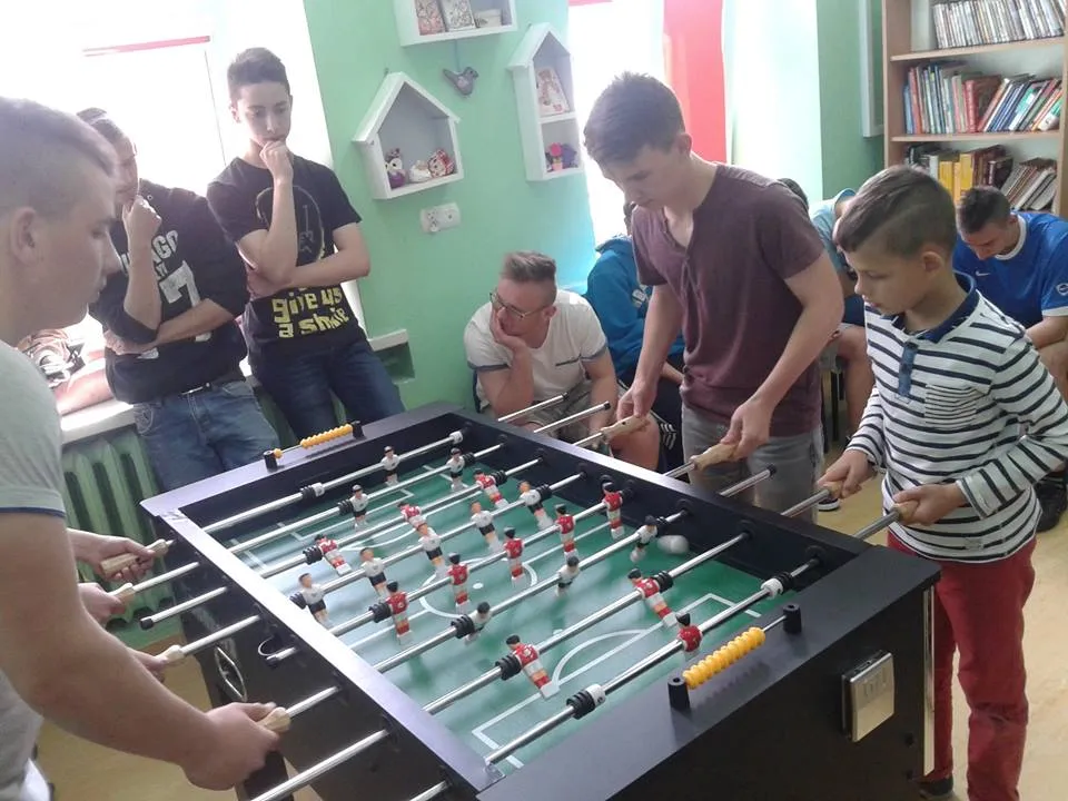 Na zdjęciu widnieje kilku chłopców z placówki grających w piłkarzyki na specjalnym do tego stole.