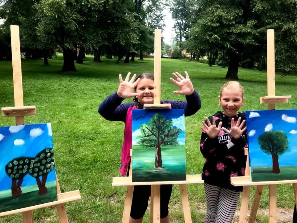 Obraz przedstawia dzieci wraz z swoimi obrazami wykonanymi przy użyciu akryli.