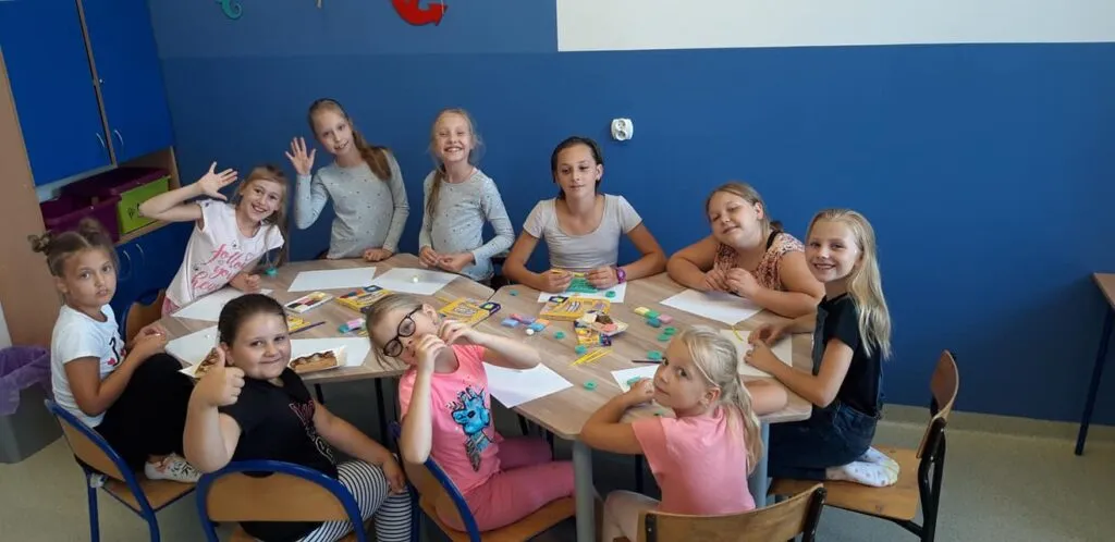 Obraz przedstawia wychowanków SPWD podczas zajęć artystycznych, na których malują, rzeźbią, czy projektują modelinowe breloczki.