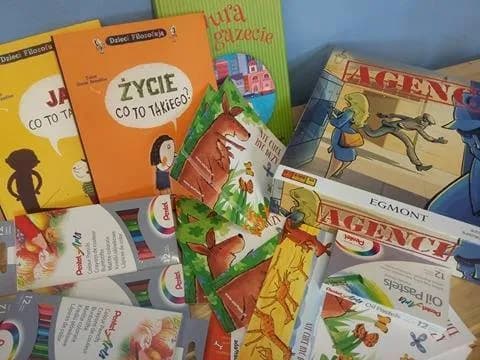 Zdjęcie przedstawia kredki, książki oraz gry planszowe rozłożone na stole.