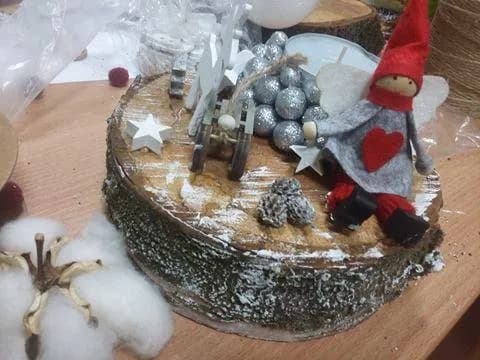 Obraz przedstawia pień drzewa ozdobiony przy użyciu sztucznego śniegu, na którym znajdują się m.in. szyszki, gwiazdki, bombki, czy Aniołek.