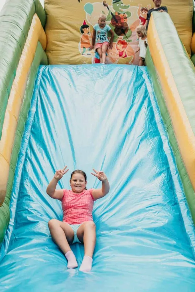 Obraz przedstawia wychowanków bawiących się na dmuchanej zjeżdżalni podczas pikniku.