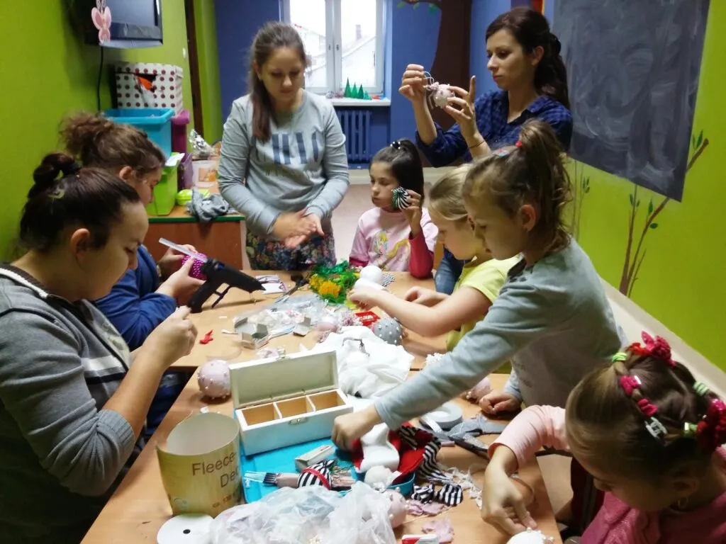 Zdjęcie przedstawia dzieci z placówki w sali zajęciowej z zielonymi ścianami, robiące dekoracje z okazji zbliżających się świąt.