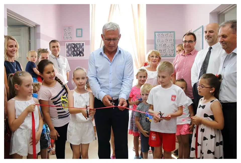 Obraz przedstawia uroczyste przecięcie czerwonej wstęgi przez burmistrza gminy Radłów oraz wychowanków SPWD.