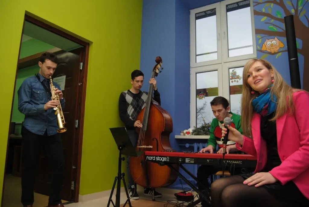 Obraz przedstawia osoby grające na instrumentach oraz śpiewające.