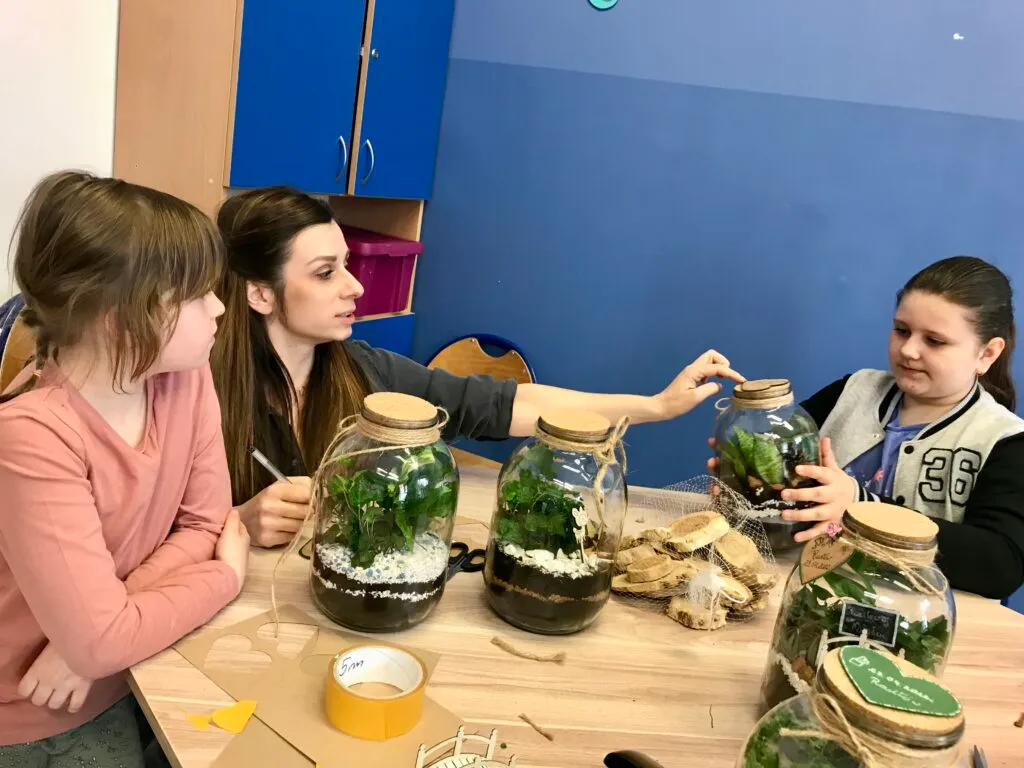 Dzieci z opiekunką tworzące dekoracje przy stole w niebieskim pokoju